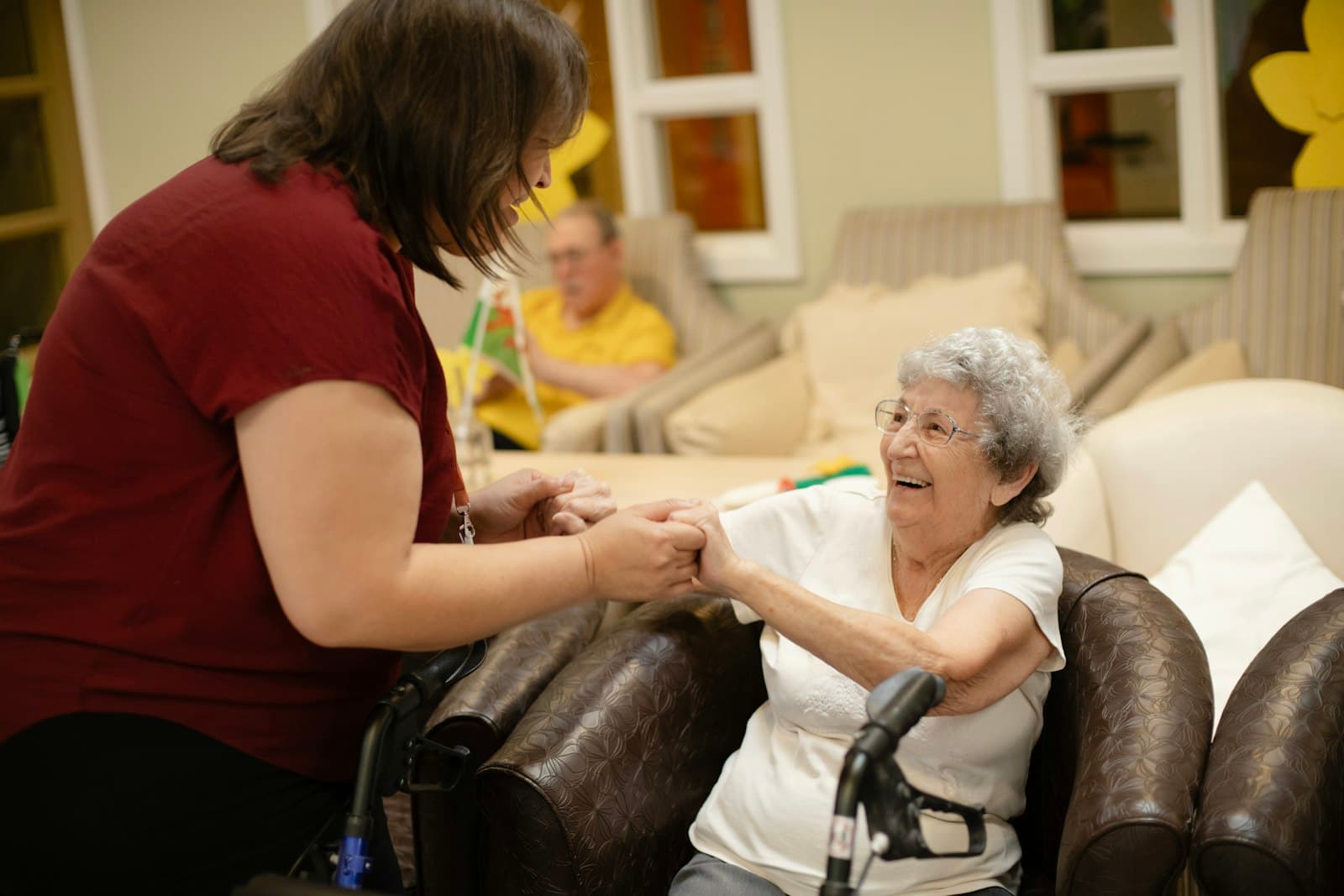 A carer holding hands with a smiling older woman in her chair
